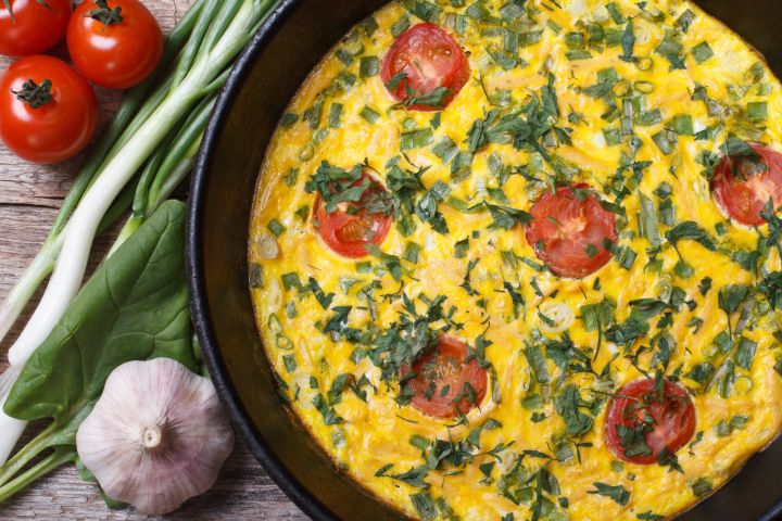 Baked frittata with tomatoes and goat cheese in a skillet with fresh herbs. 