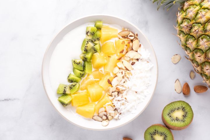 Tropical yogurt bowl with sliced pineapple, kiwi, almonds, and shredded coconut layered in a bowl.