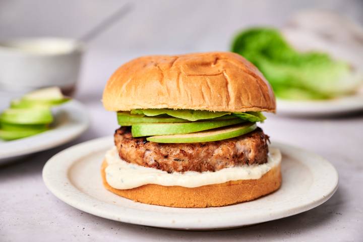 Turkey Apple Burgers on a bun with sliced green apples, lettuce, and yogurt sauce.