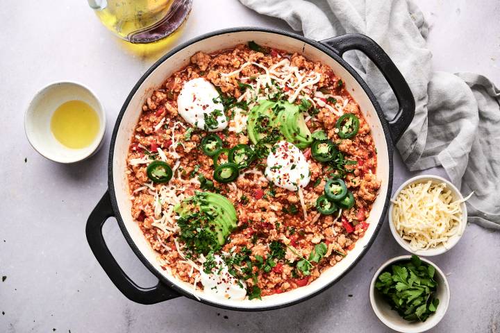 Ground turkey and cauliflower rice taco skillet with jalapenos, sour cream, cilantro, and lime wedges.