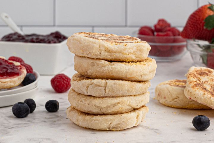Two ingredient English muffins stacked on a marble board with fresh berries and jam on the side.