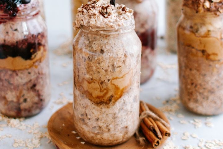 Vanilla latte overnight oatmeal with cinnamon in a glass jar with a touch of whipped cream on top.