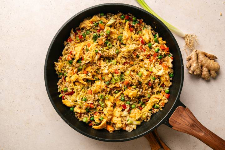 A black pan filled with colorful fried rice, featuring peas, carrots, scrambled eggs, and green onions.