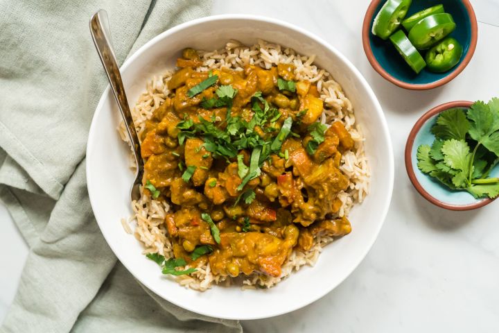 Vegetable korma with potatoes and carrots in a creamy tomato coconut curry sauce on a plate with rice and cilantro.