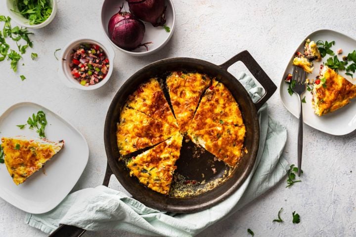 Western omelet frittata with peppers, onions, ham, and cheese cooked in a cast iron skillet and served with fresh parsley.