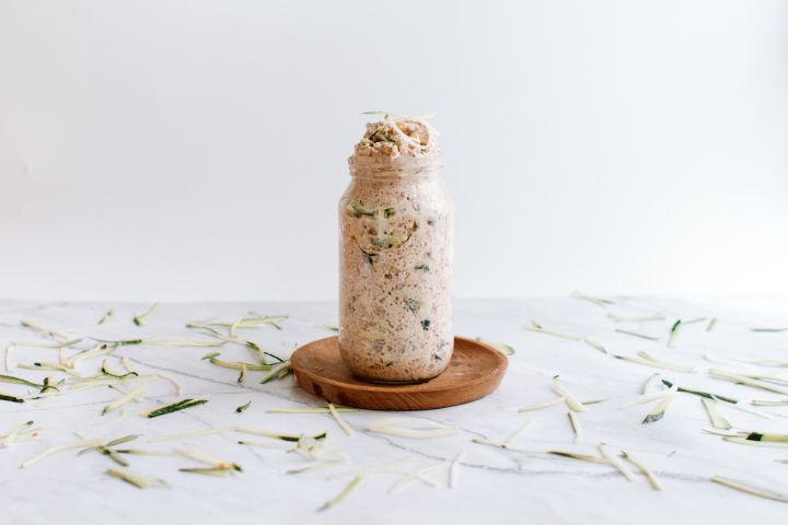 Zucchini bread overnight oatmeal in a glass jar with cinnamon, rolled oats, almond butter, and shredded zucchini.