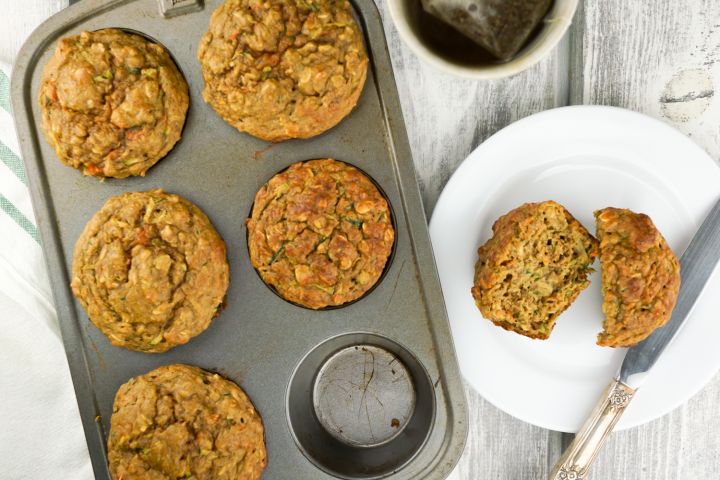 Zucchini carrot muffins in a muffin tin with one on a plate.