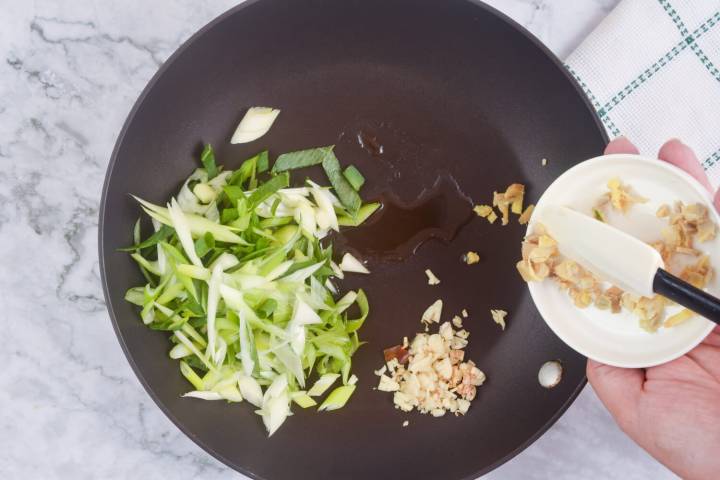 Green onions, garlic, ginger,. and sesame oil cooking in a pan.