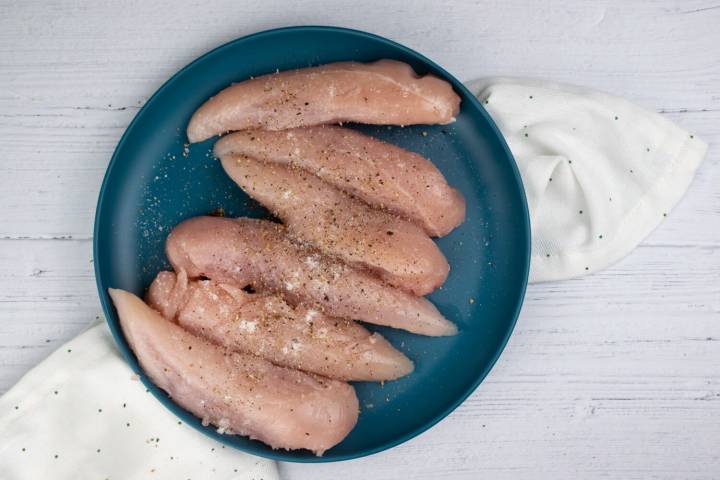 Chicken breast with garlic powder, salt, and pepper on a blue plate.