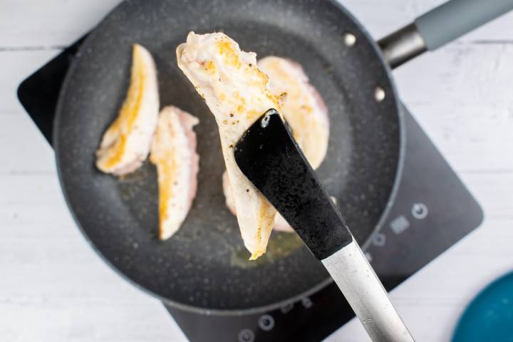 Chicken breast tenderloin being flipped with tongs in a pan.