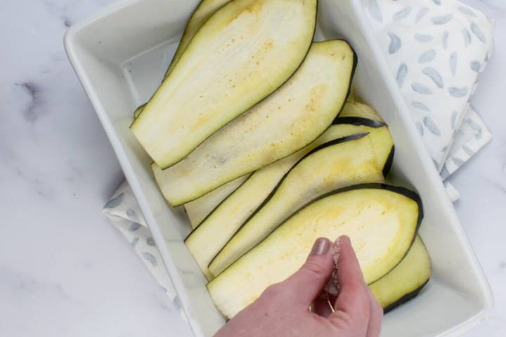 Sliced eggplant being sprinkled with salt.
