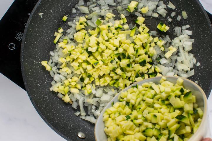 Zucchini and onions being sauteed in a pan.