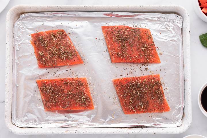 Salmon fillets on a baking sheet coated with olive oil and spices.