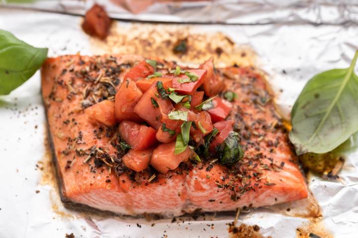 Baked Italian salmon on a baking sheet with chopped tomatoes, basil, and balsamic vinegar.