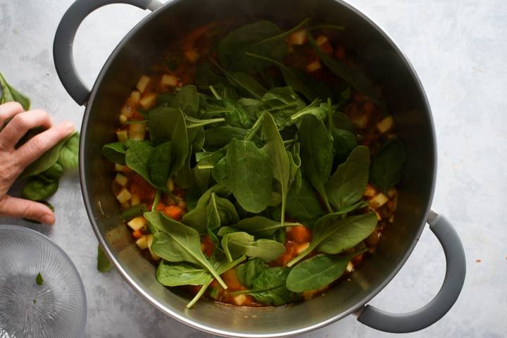 Spinach being added to a pot of bean and vegetable soup.