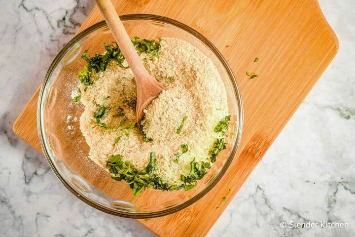 Breadcrumbs, parmesan cheese, basil, oregano, and garlic powder in a bowl with a wooden spoon.