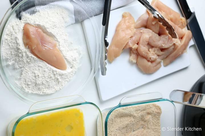 Chicken tenders being dipped in flour and breadcrumbs.