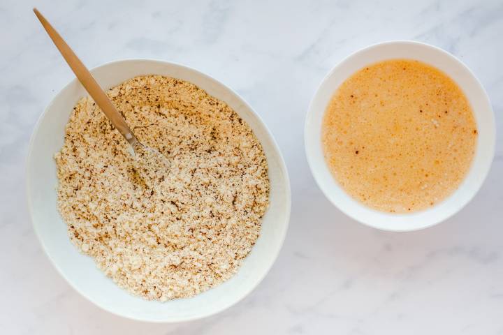 Almond flour mixed with flaxseed, salt, and baking soda in a bowl and a bowl with whisked eggs.