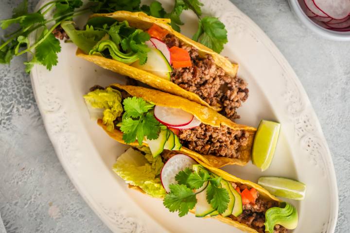 Ground beef with taco seasoning being added to corn tortilla shells.