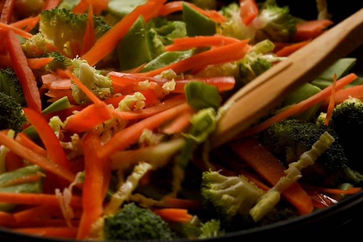 Ginger and garlic being stirred into a pan of stir fried vegetables.