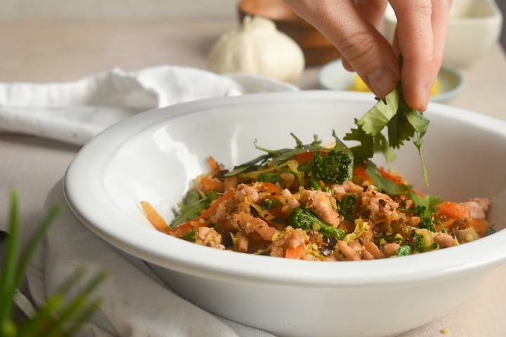Asian quinoa and turkey stir fry being topped with cilantro in a bowl.