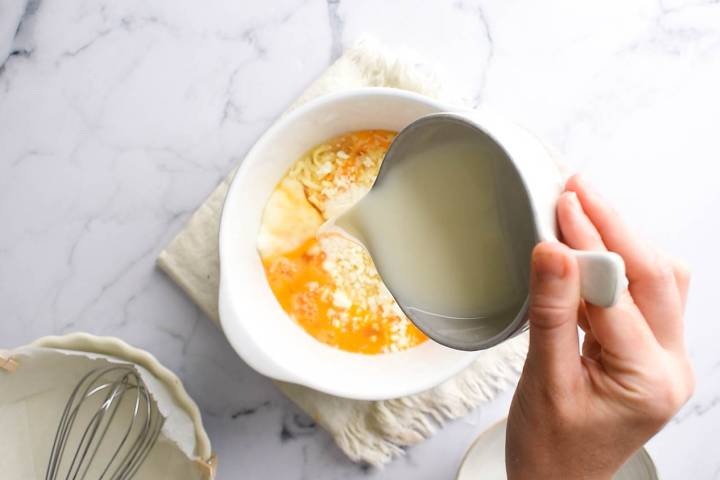 Eggs, milk, mozzarella cheese, feta cheese being whisked in a bowl.