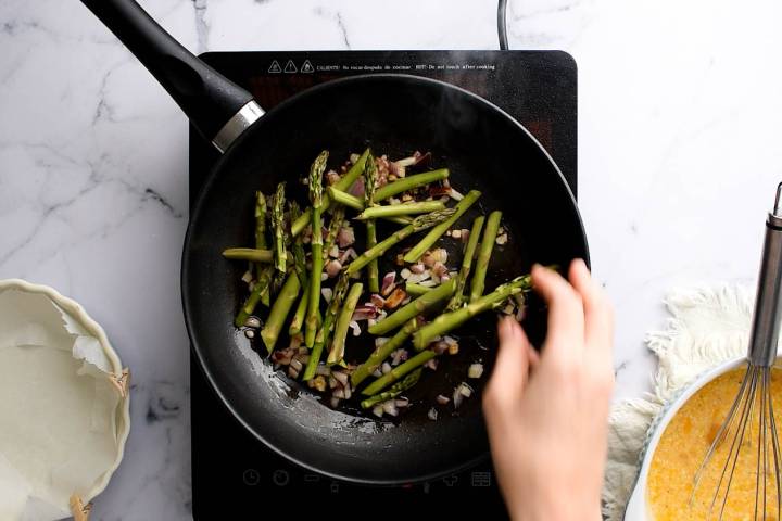 Asparagus and red onion cooking in olive oil in a skillet.