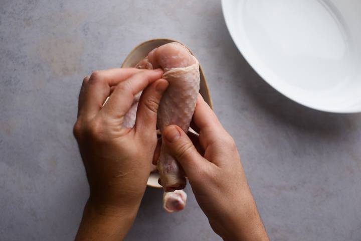Hands removing the skin from chicken drumsticks.