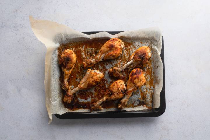 Baked chicken drumsticks coated with spices on a baking sheet with parchment.