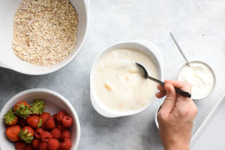 Milk, eggs, bananas, and maple syrup being stirred in a bowl.