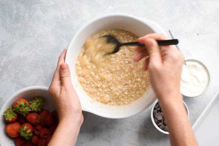 Rolled oats being combined with milk, bananas, and eggs in a bowl.