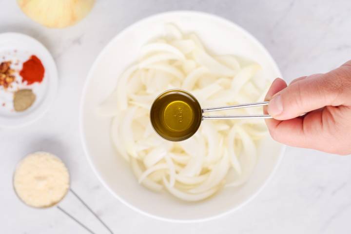 Onions in a bowl being tossed with olive oil and spices.