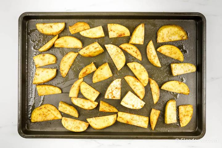 Potato wedges spread out o a baking sheet.