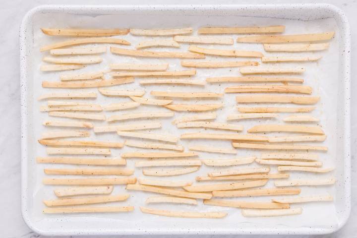 Thinly sliced turnips and potatoes on a baking sheet in single layer.