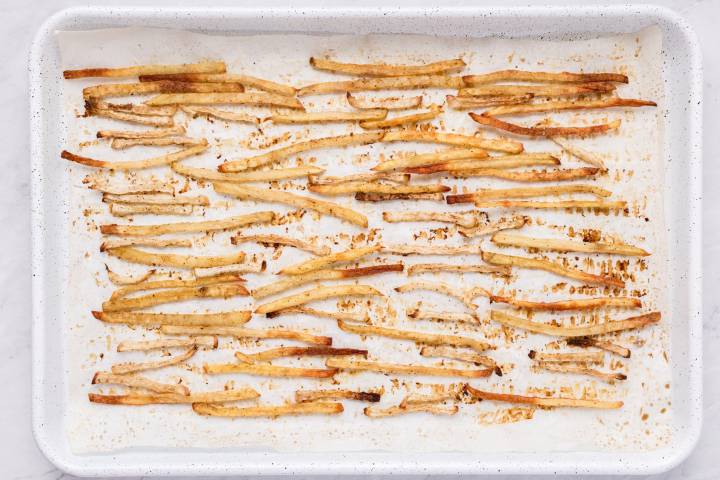 Crispy baked fries on a white baking sheet with parchment paper.