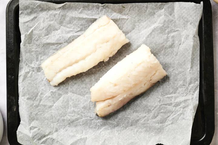Haddock fillets on a baking sheet covered in parchment paper.