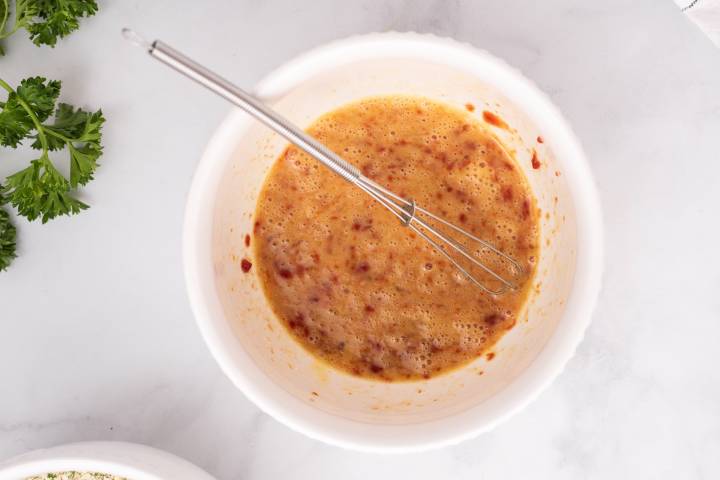 Egg and tomato paste being whisked in a bowl.