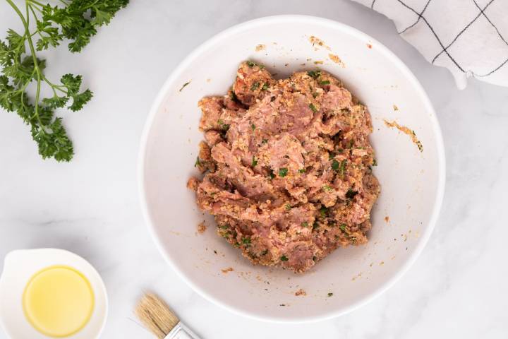 Ground turkey, breadcrumbs, eggs, cheese, and spices being mixed for meatballs in a bowl.