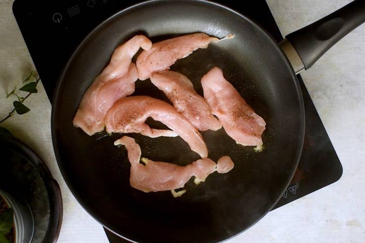 Chicken breast tenderloins being seared in a skillet.