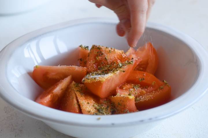 Tomatoes being tossed with garlic powder, oregano, salt, and pepper.