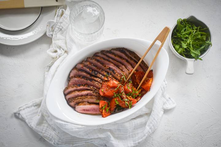 Cooked balsamic flank steak sliced and served sliced tomatoes and herbs.