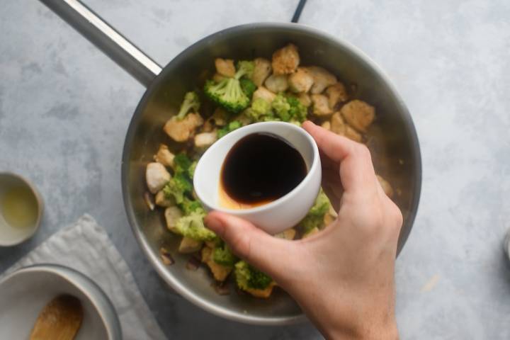 Soy sauce being added to a pan with chicken breast and broccoli.