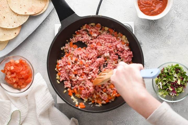 Ground beef cooking with peppers and onions in a skillet.