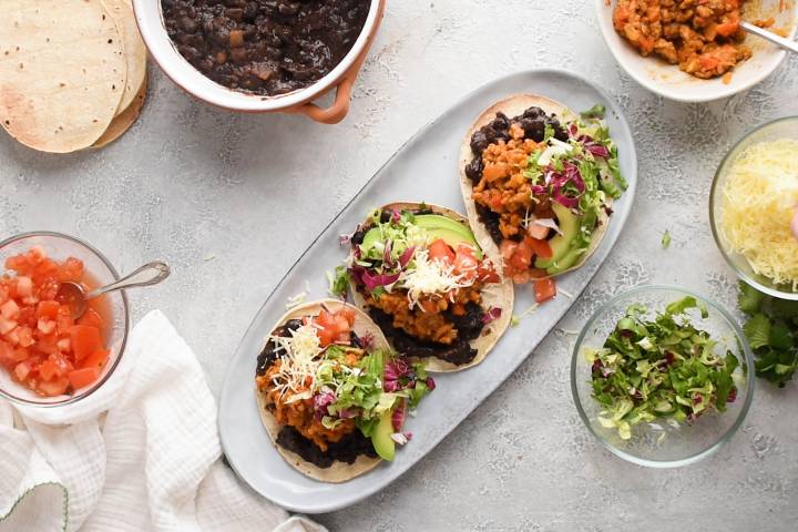 Cheese being added to three ground beef tostadas.