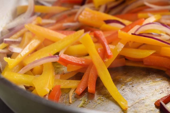 Sliced peppers and onions cooking in a skillet.