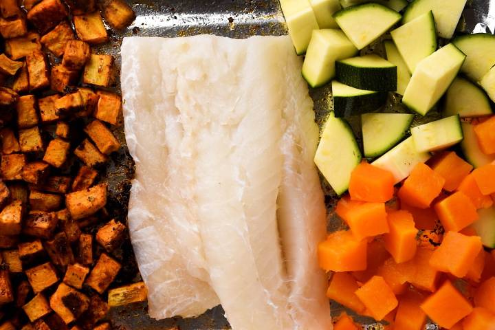 Cod, sweet potatoes, zucchini, and butternut squash on a baking sheet.