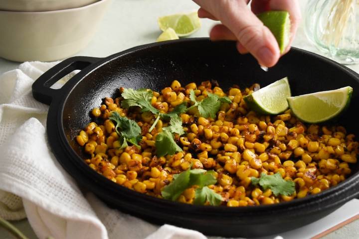 Blackened corn in a skillet with cilantro and fresh lime being squeezed on top.