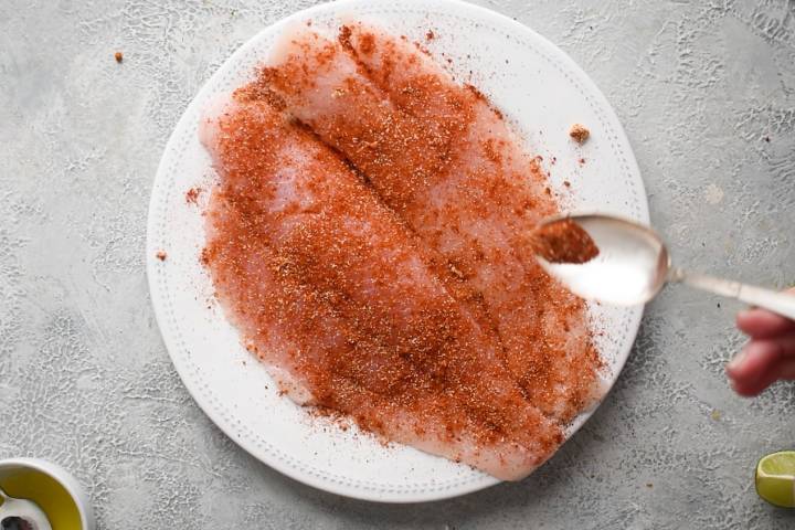 Fish coated with seasoning on a white plate.