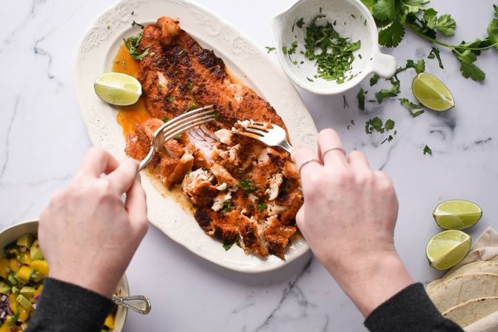Blackened fish being flaked into pieces by two forks.