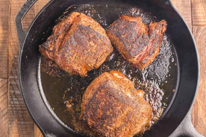 Steak with seasoning being blackened in a cast iron skillet.